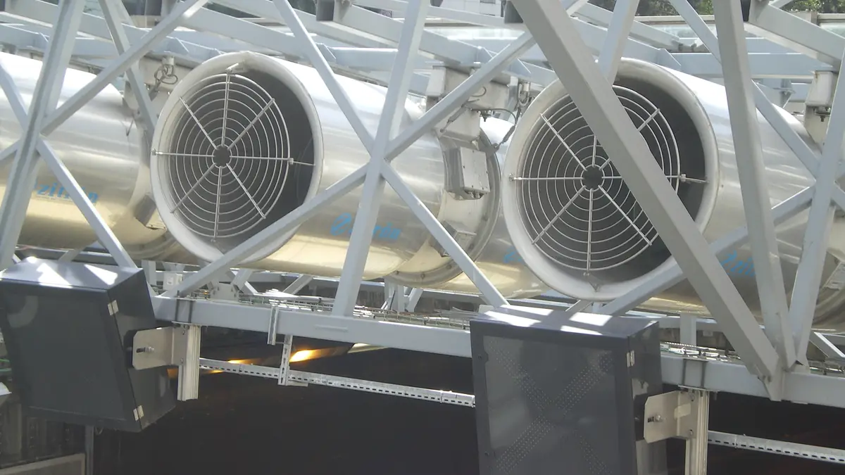 Portal de un túnel vial con ventiladores de chorro suspendidos y bandejas portacables a lo largo del hastial.