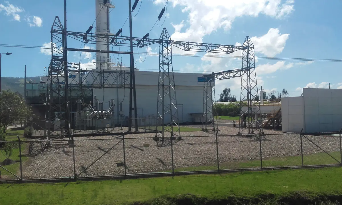 Subestación eléctrica al aire libre detrás de una cerca, con transformadores y estructuras de barras.
