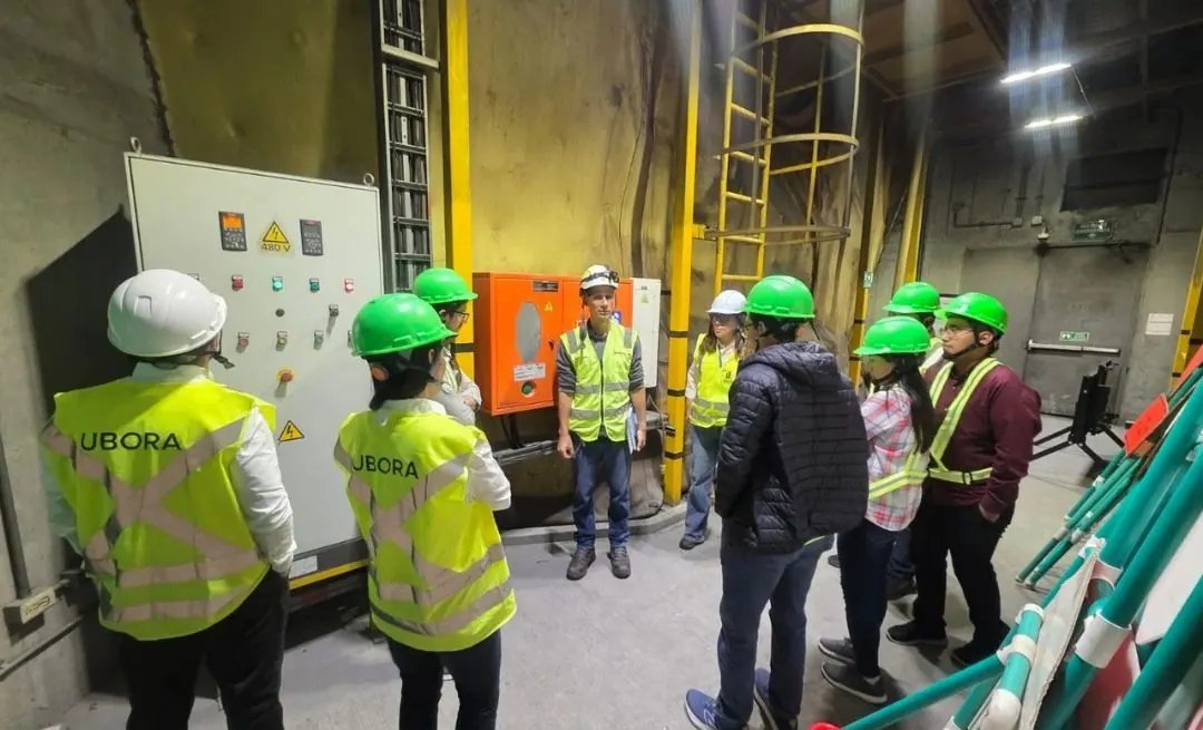 Personas con chaleco de UBORA, de espaldas, observan un tablero eléctrico en una galería del túnel.